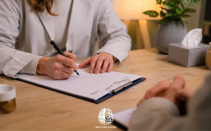 Một chuyên gia đang ghi chú trong buổi tham vấn, chỉ thấy tay và sổ ghi chép, không lộ mặt thân chủ; không khí chuyên nghiệp, bảo mật, ấm áp] | [GAD-7 là công cụ sàng lọc rối loạn lo âu lan tỏa