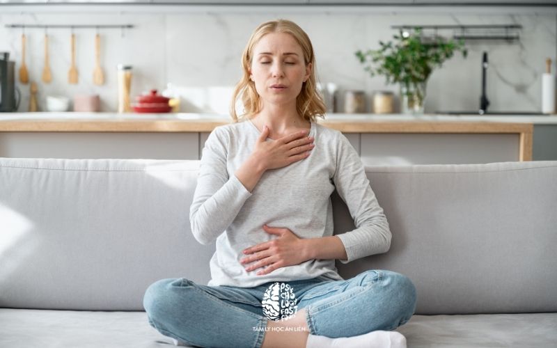 Hình ảnh người phụ nữ nhắm mắt thực hành hít thở sâu, tay ôm nhẹ lên ngực | Kỹ thuật thở bụng 4-7-8 giúp giảm tim đập nhanh khó thở